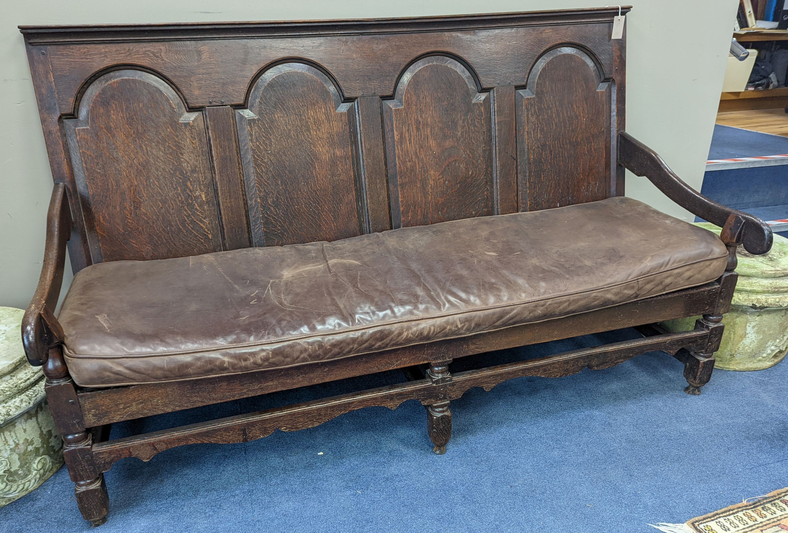 A mid 18th century panelled oak settle with leather squab seat, length 185cm, depth 77cm, height 114cm
